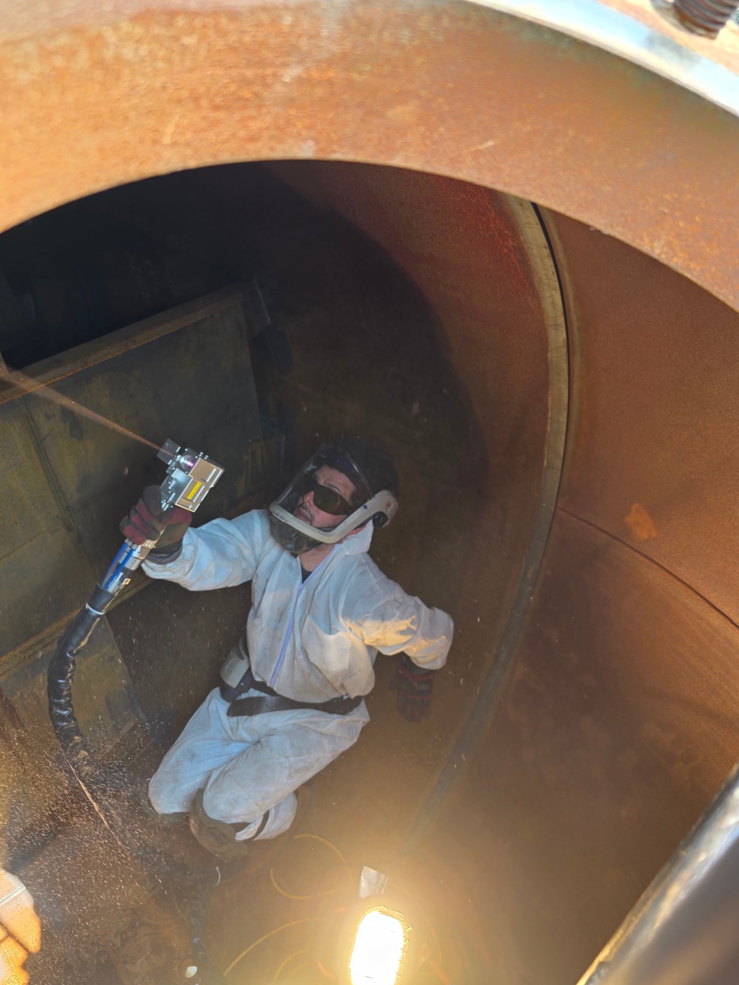 Technician in protective suit using laser equipment to clean corroded vessel interior