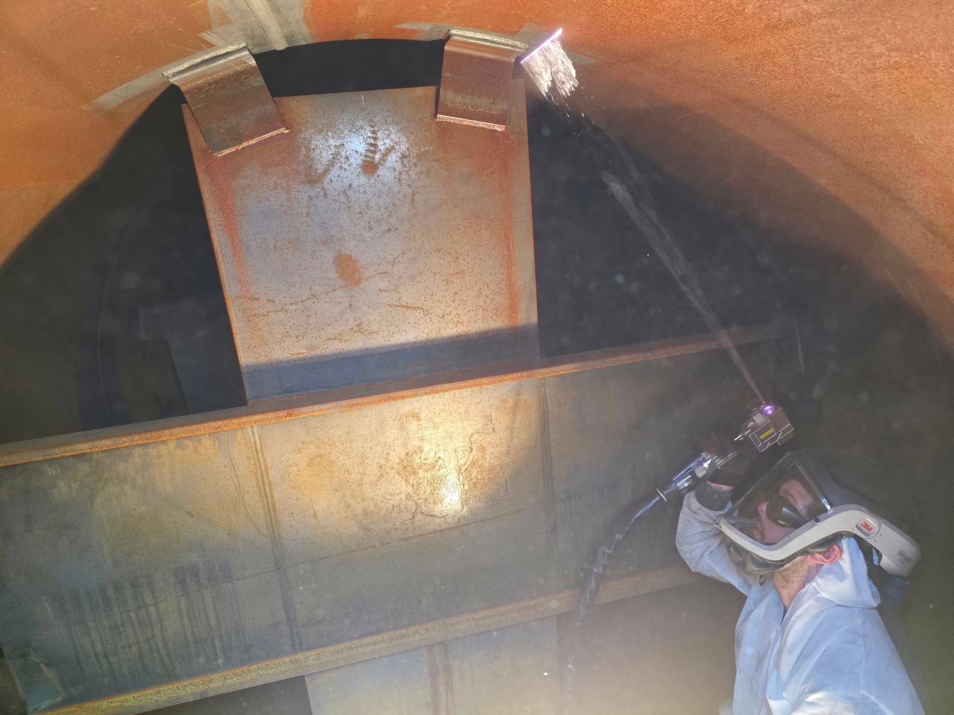 Worker in protective suit using laser decontamination tool inside industrial vessel