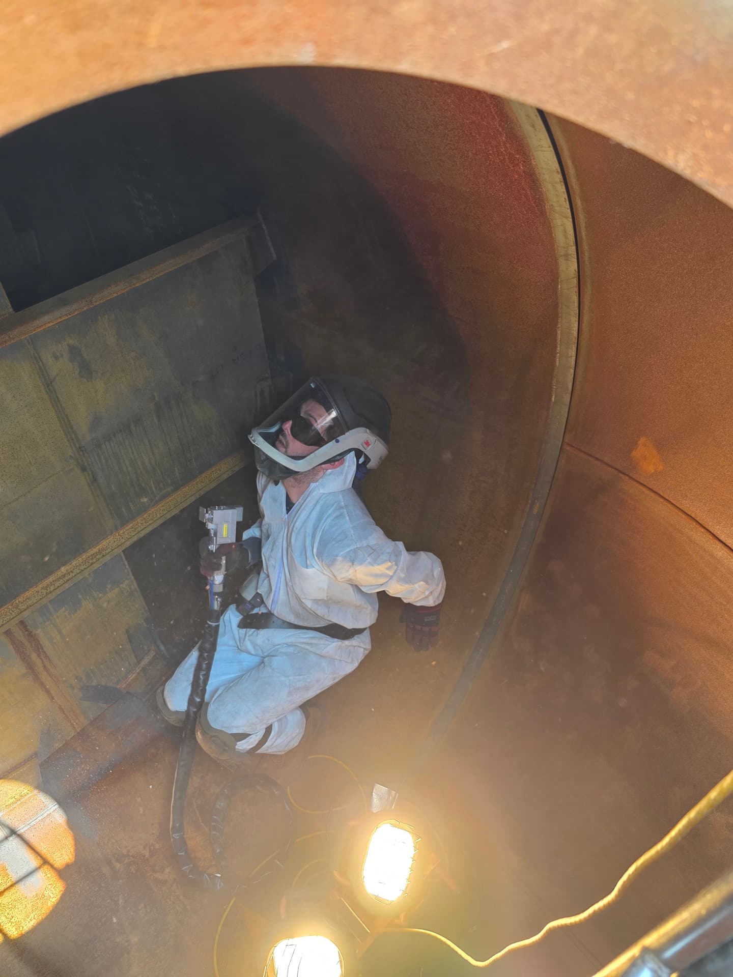 Close-up of decontamination specialist with laser equipment inside industrial vessel