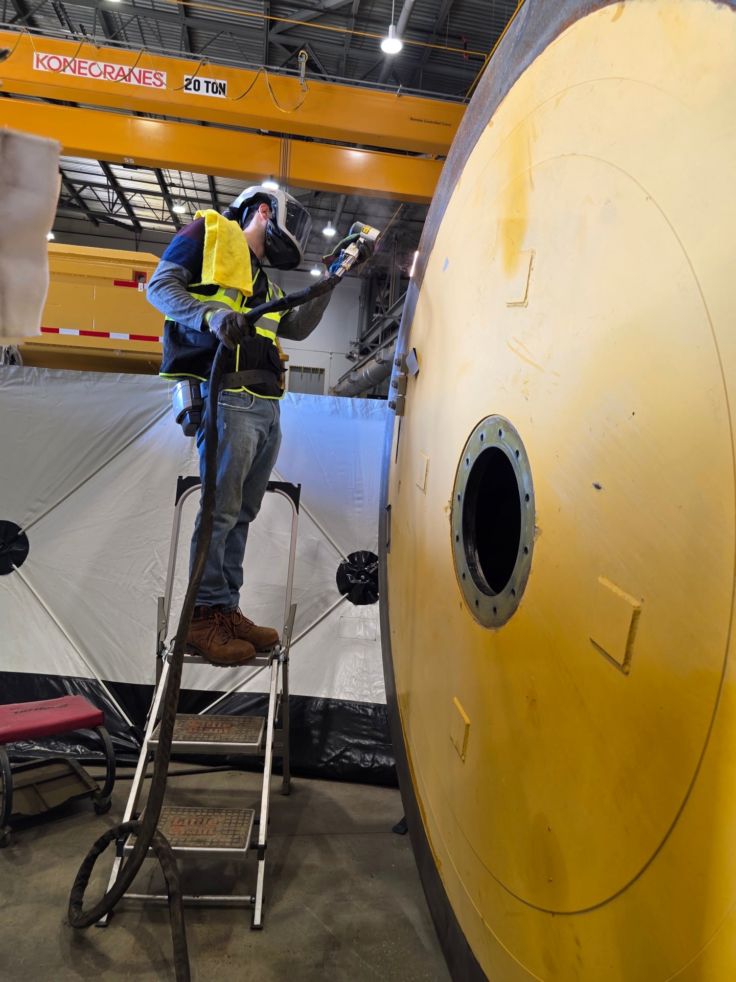 Worker in safety vest inspecting large industrial pressure vessel component in facility
